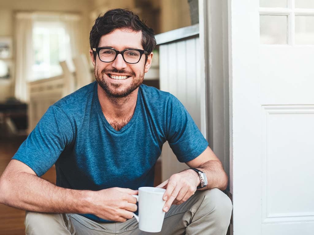 Mees prillidega ja sinises särgis istub põrandal, hoides lõdvestunult käes kohvitassi