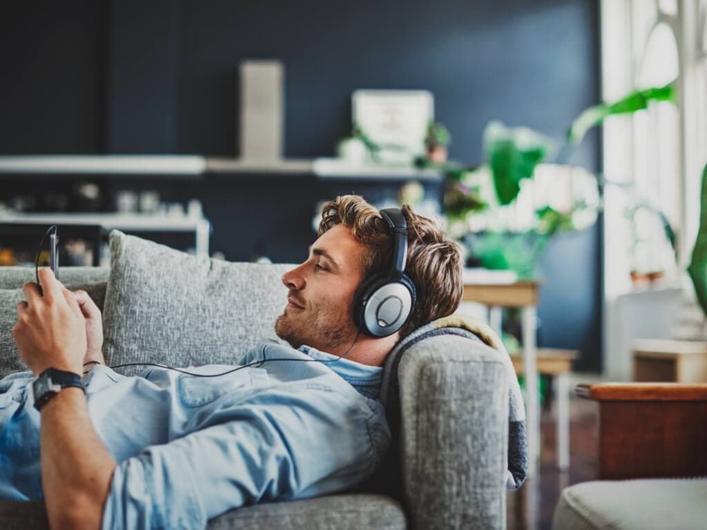 Mees lõõgastub diivanil, kuulates muusikat kõrvaklappidega, rahuliku ilmega