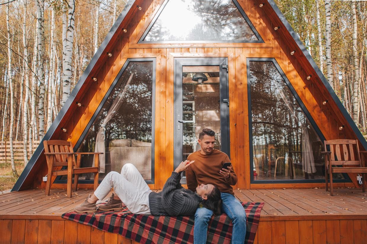 Paarike istub pingil, naeratades, väikese võluva maja ees, mida ümbritseb rohelus